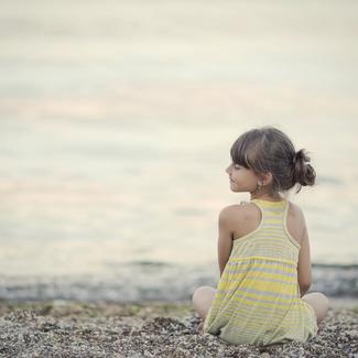 Girl sitting on a pebble beach, smiling towards the water