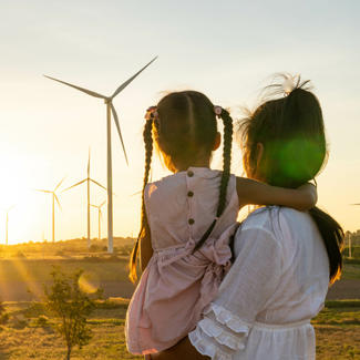 Caregiver holds child as they look at a field of windmills during a sunset
