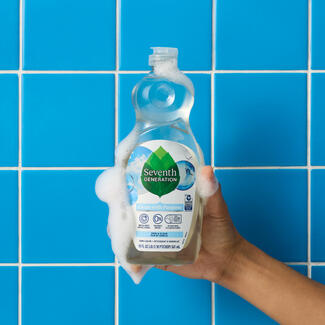 Hand is holding Seventh Generation Free and Clear dishwashing liquid bottle against blue tile background